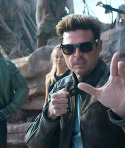 Karl Urban as Johnny Cage strikes a martial arts pose in the trailer for Mortal Kombat II as two characters stand behind him in the background
